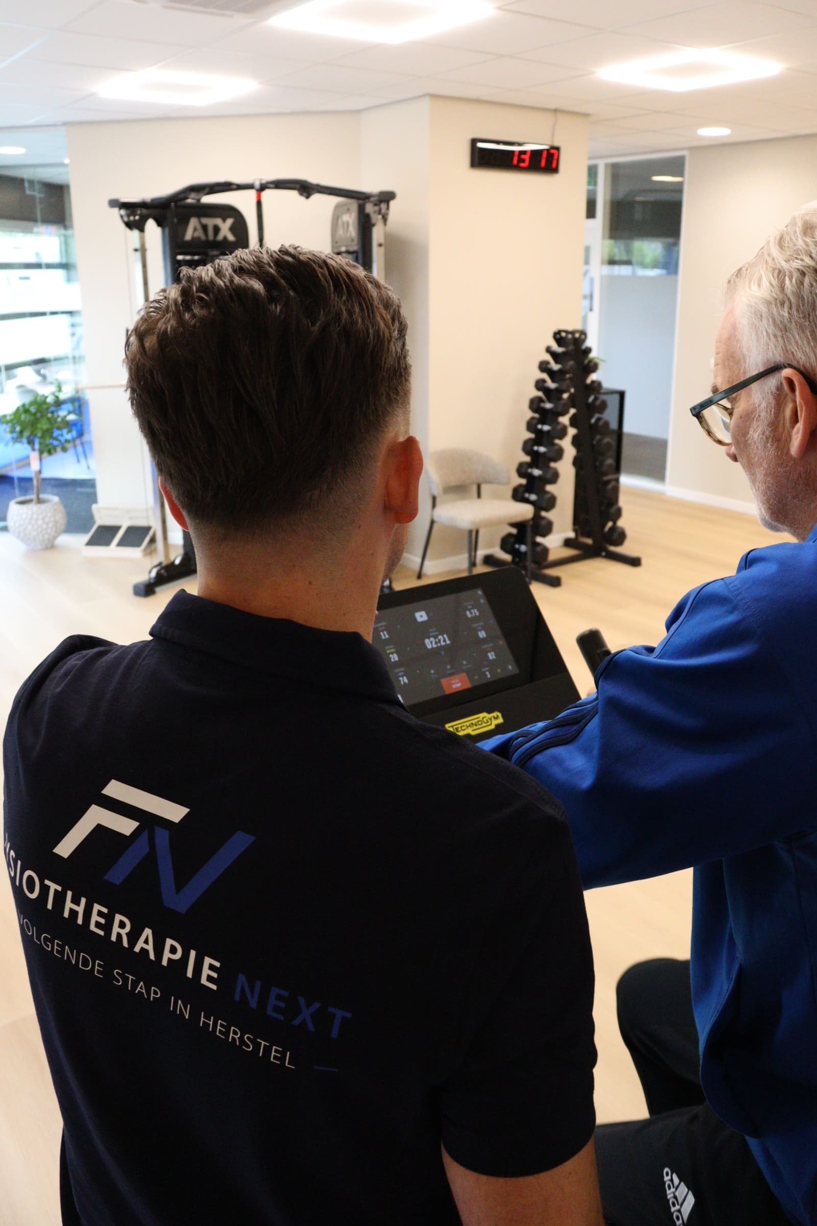 Fysiotherapeut begeleidt een client bij een oefening op de hometrainer