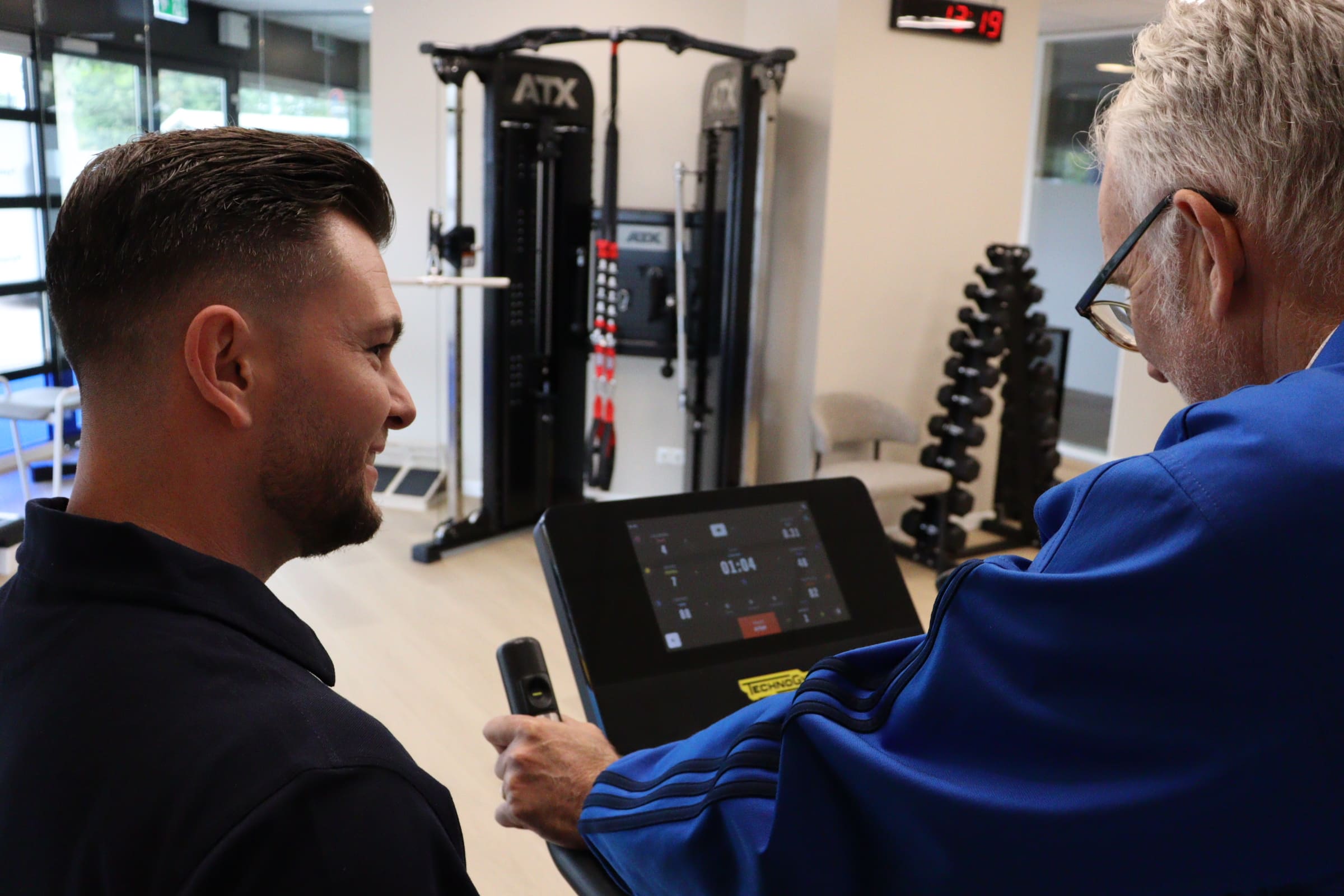 Fysiotherapeut en client in gesprek bij een trainingstoestel