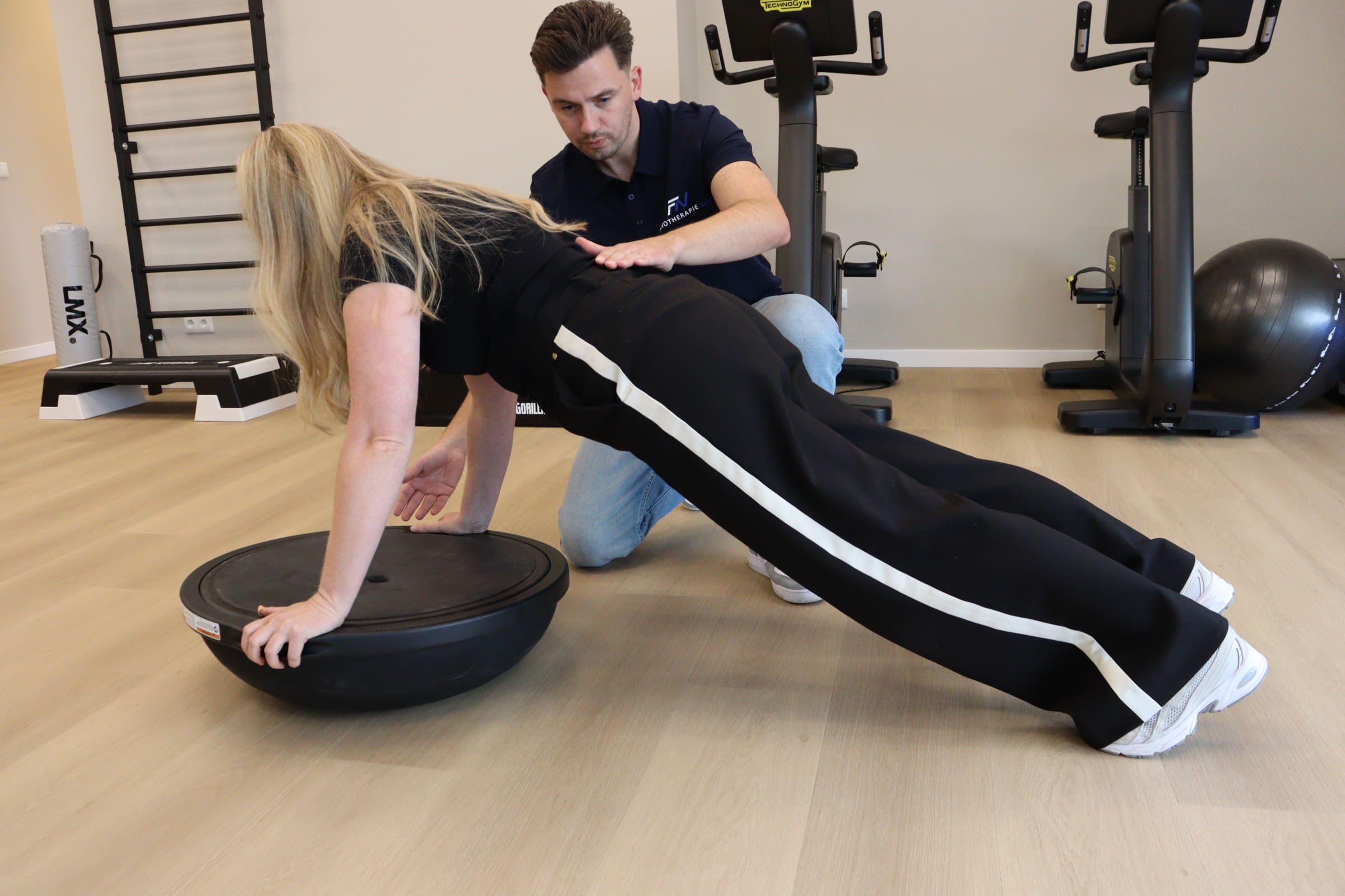 Personal trainer begeleidt een client bij een plankoefening op een balansbal